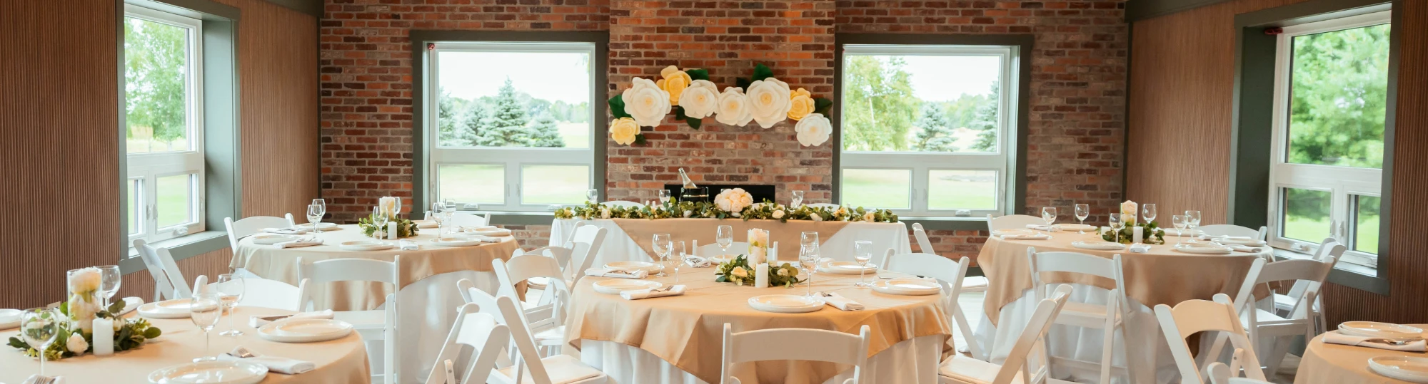 Wedding reception venue featuring head table surrounded by round tables with white table cloths.